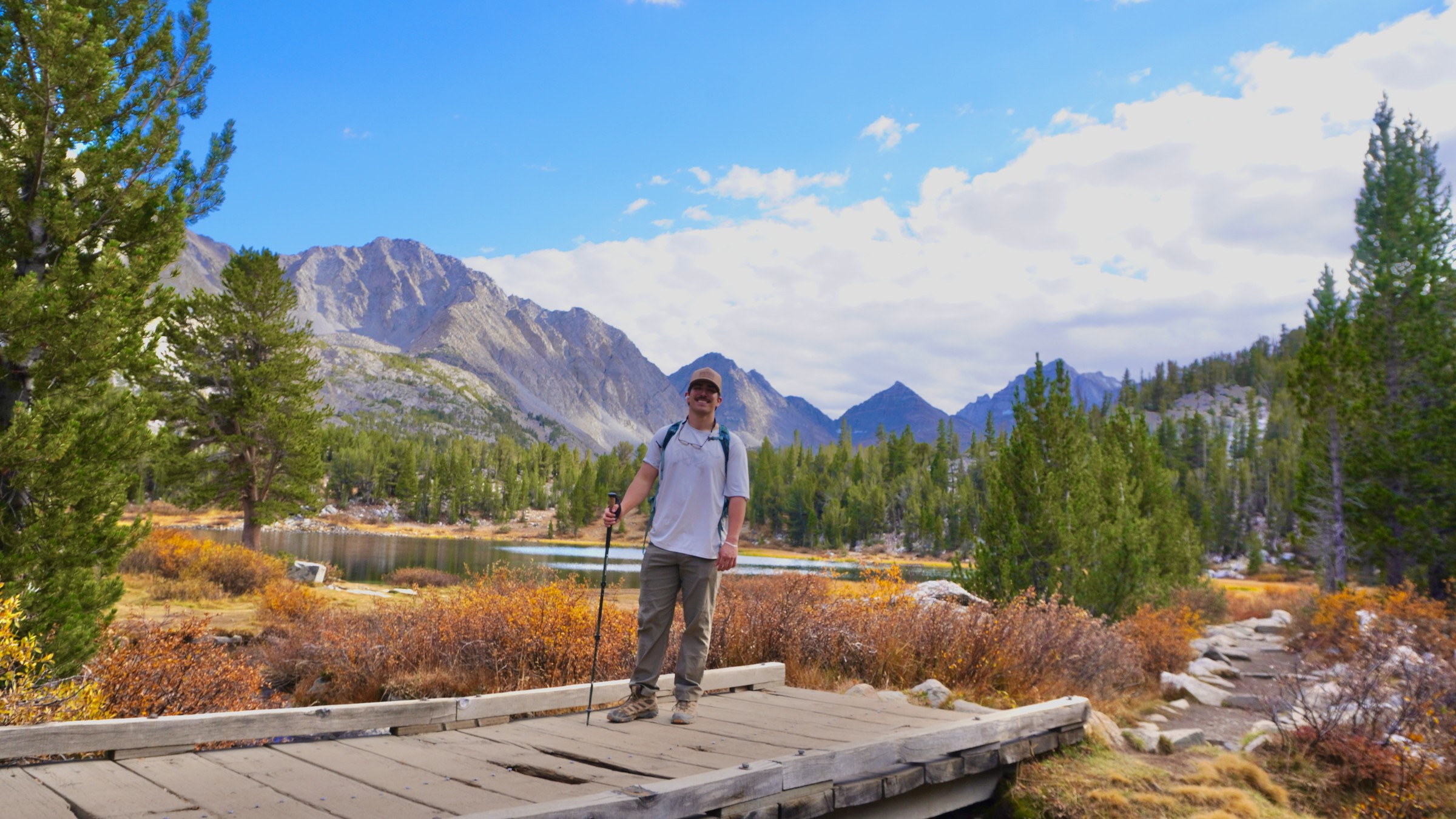 Tim Yslava standing on a wooden footbridge beside the second lake on the Little Lakes Valley hike, with granite peaks behind him
