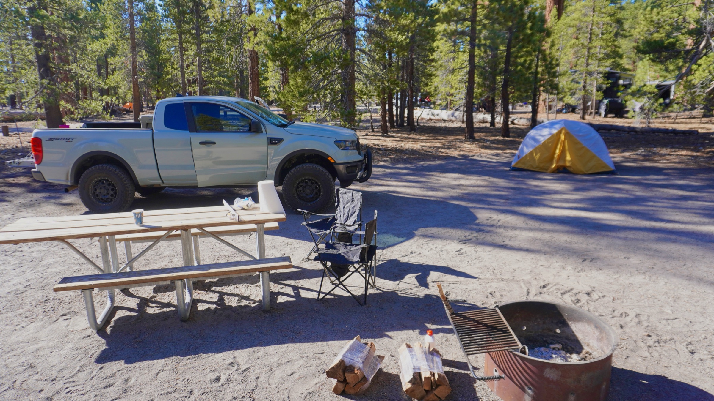 Pickup truck, tent, picnic table, camp chairs, fire ring, and firewood at an Eastern Sierra campsite
